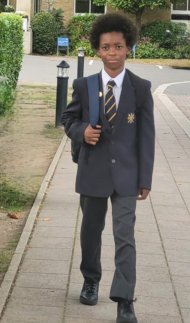 Lisa's son on his first day at private school, in blazer and tie with his school bag over one shoulder