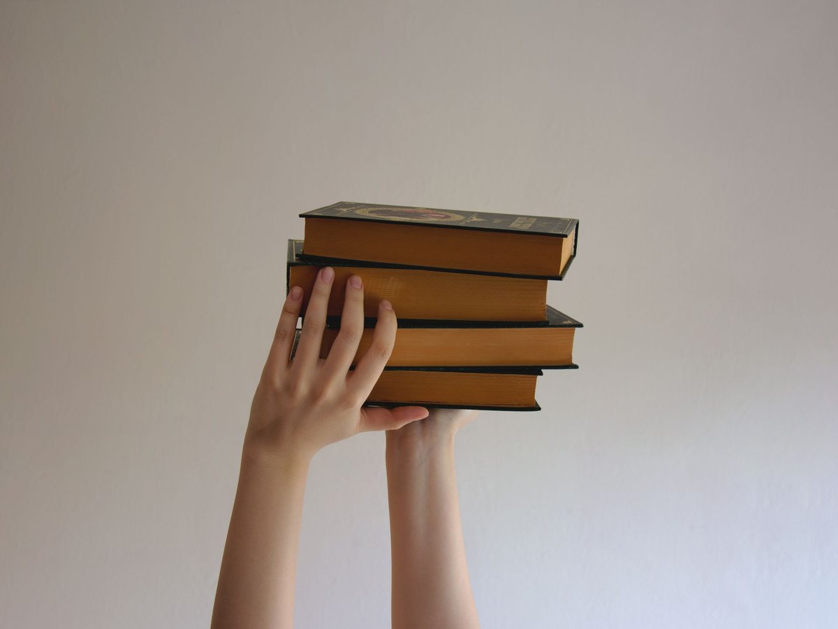 A pair of hands holding up a stack of hardback books